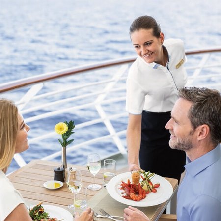 Restaurantfachfrau an Bord von Hapag-Lloyd Cruises serviert mit Blick auf das Meer