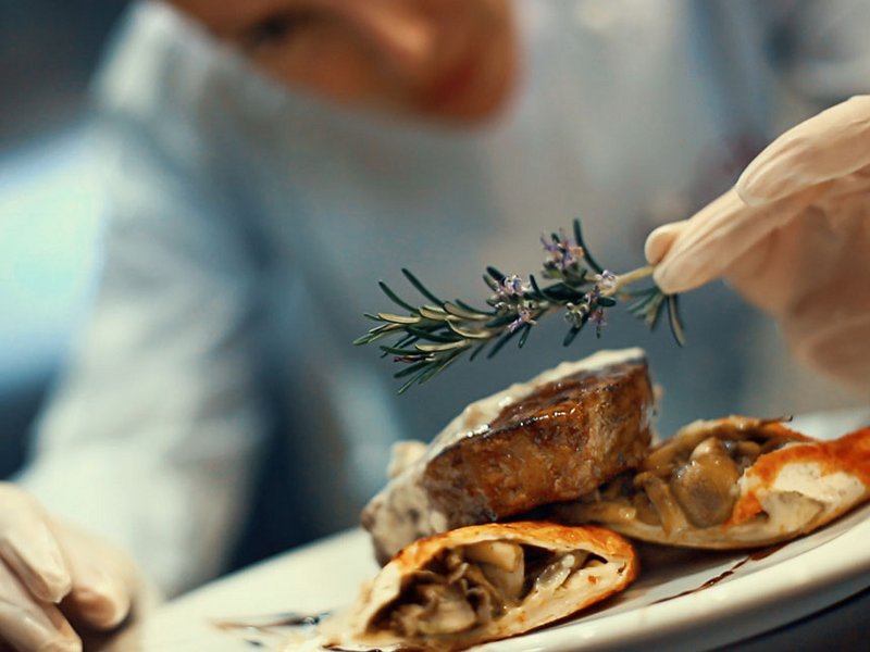 Koch legt vorsichtig Rosmarin auf einen anferichteten Teller
