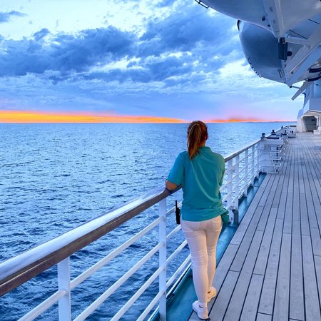 Crewmitglied auf MS Amera von Phoenix Reisen an der Reling von hinten bei Sonnenuntergang auf See
