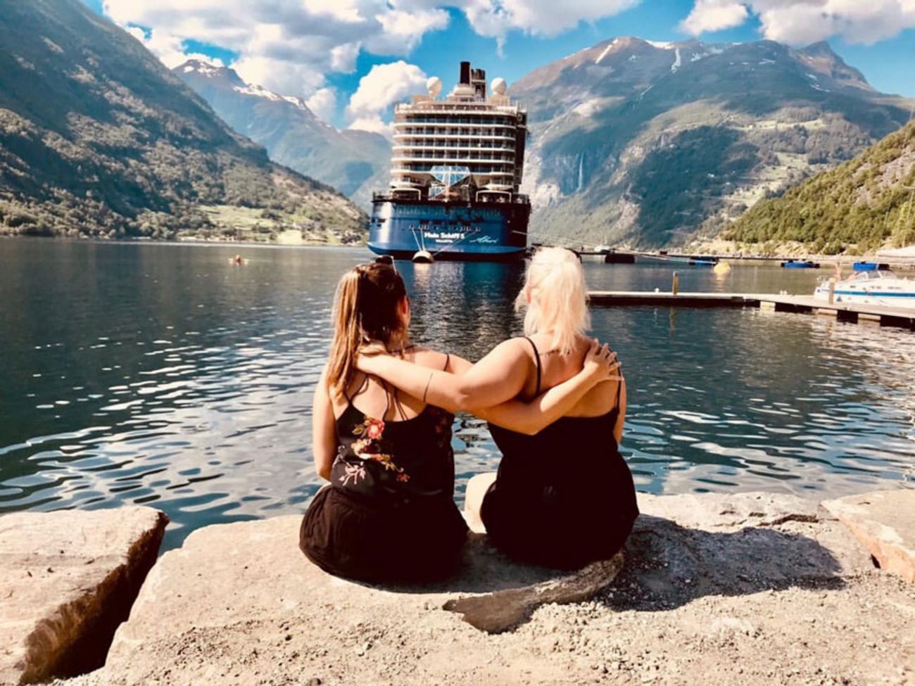 Arbeitgeber sea chefs – Vorteile & Services (Crew): Family & Friends Crew-Mitglieder in Freizeitkleidung sitzen vor Mein Schiff am Ufer in einem Fjörd