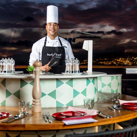 Koch auf Mein Schiff macht live cooking an der Reling mit Blick auf eine Insel bei Nacht