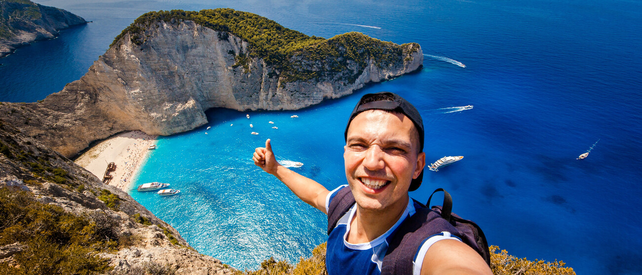 Junger Mann macht Selfie von sich im Hintergund blaues Meer und Steilküste