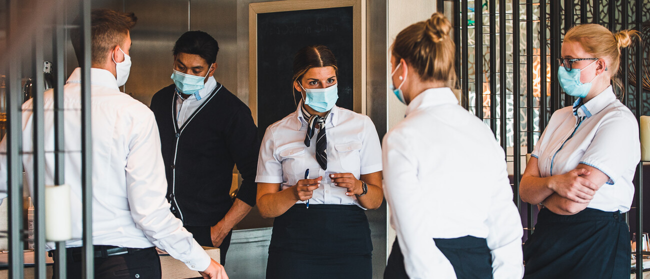 Kreuzfahrt-Crew mit Mundnasenschutz kümmert sich um die Einhaltung des Hygiene-Konzeptes