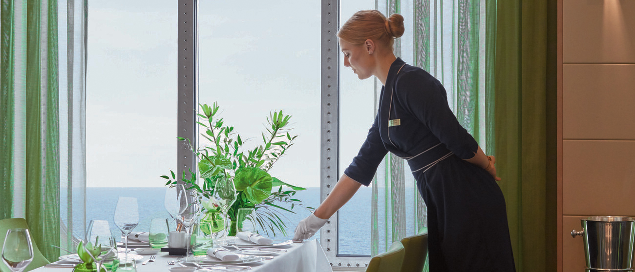 Chef de Rang auf MS EUROPA deckt einen Tisch am Fenster im Restaurant an Bord ein