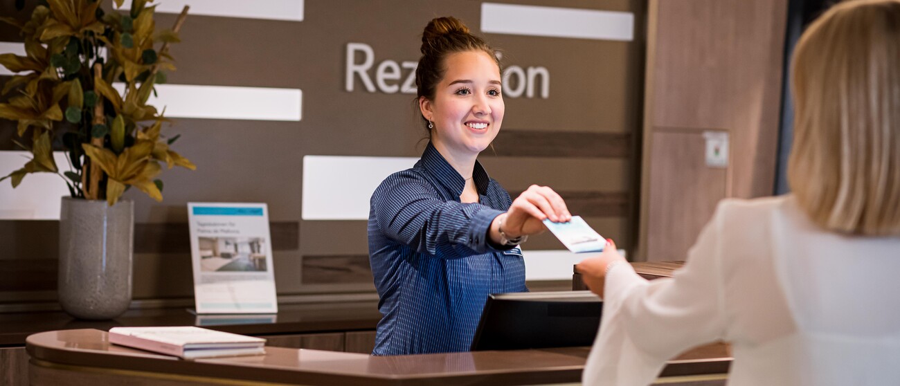 Gast erhält ZImmerkarte von lächelnder Rezeptionistin auf der Mein Schiff 2