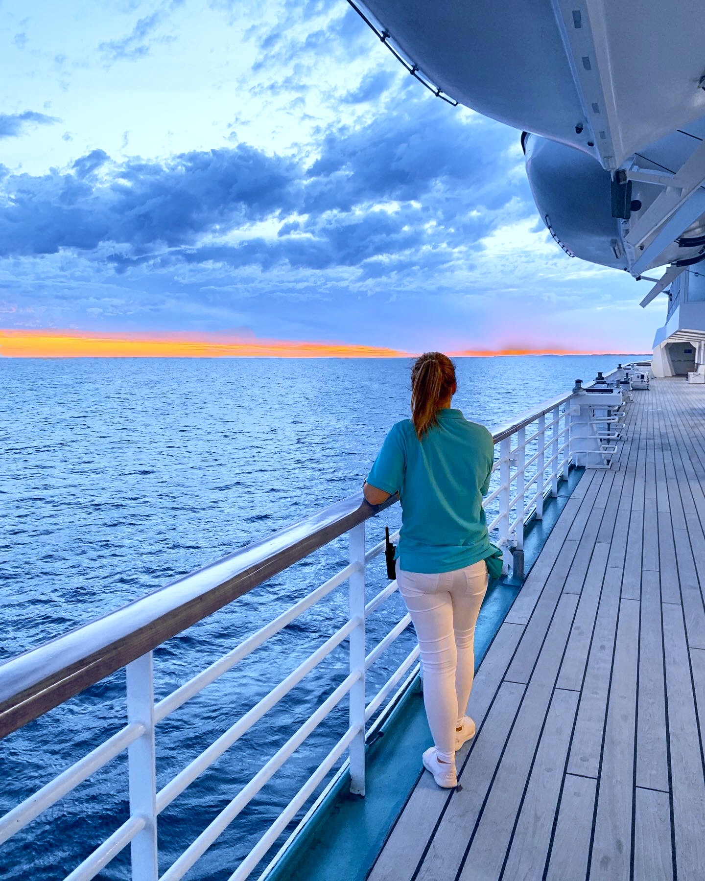 Crewmitglied auf MS Amera von Phoenix Reisen an der Reling von hinten bei Sonnenuntergang auf See