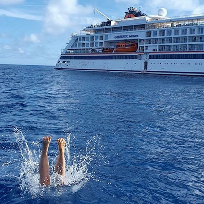 Crewmitglied der HANSEATIC nature badet im Atlantik, im Hintergrund sieht man das Schiff