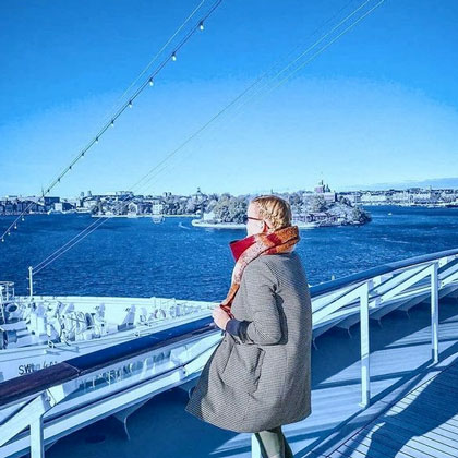 Hapag-Lloyd Cruises Crewmitglied in herbstlichem Outfit an Deck der MS Europa 2 mit Blick in schwedischen Hafen