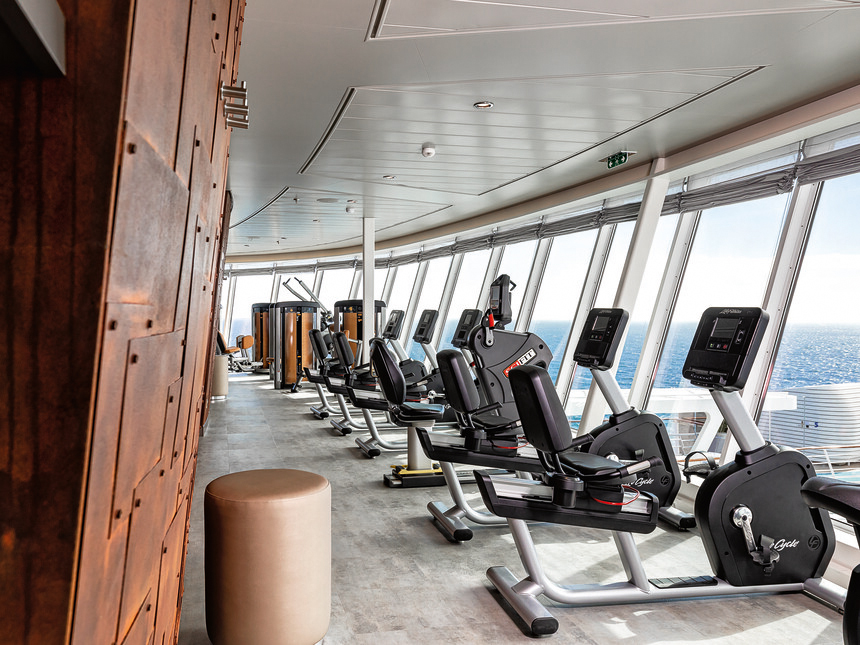 Gym auf der Mein Schiff welches von Mein Schiff Crew genutzt werden kann - unterschiedliche Trainingsgeräte vor Fenstern mit Blick auf das Meer