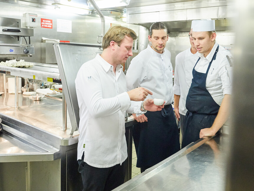 Kevin Fehling erklärt Crew Mitgliedern von MS EUROPA etwas in der Küche