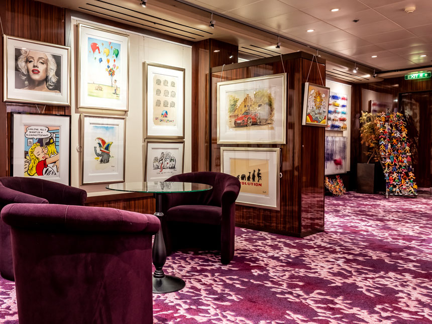 die Bilder-Gallerie an Bord der Mein Schiff Flotte, Bilder hängen an der Wand, davor lila Samt-Sessel auf lilanem Teppich