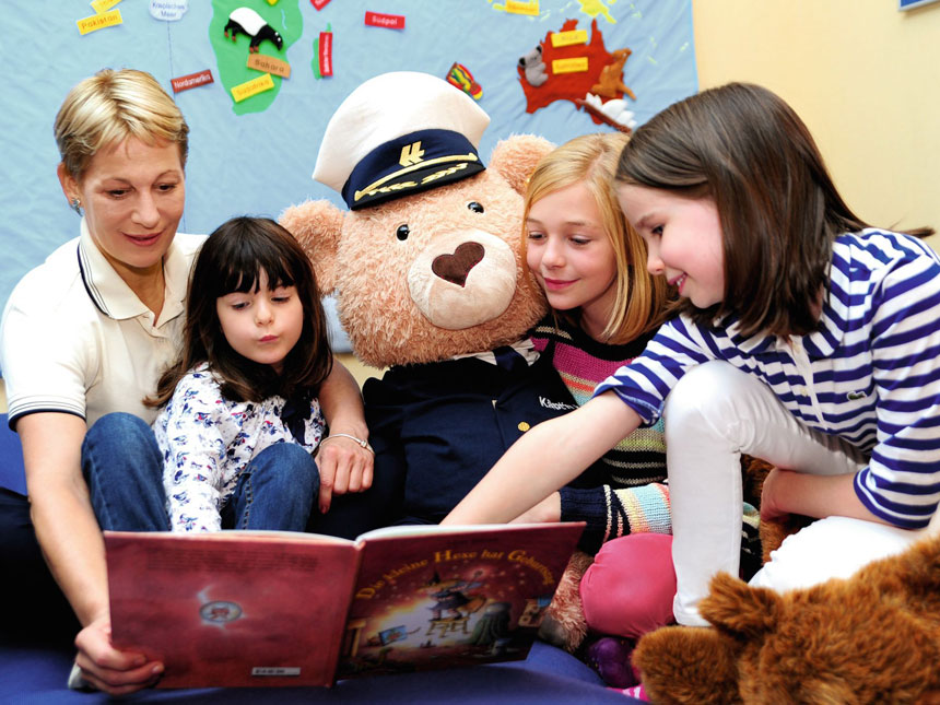 Nanny aud MS EUROPA mit großem Kuschel-Bär in Kapitänsuniform ließt Kindern etwas vor