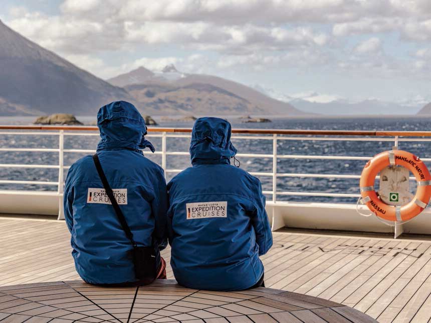 Crew Mitglieder auf HANSEATIC nature sitzen an der Reling in Jacken