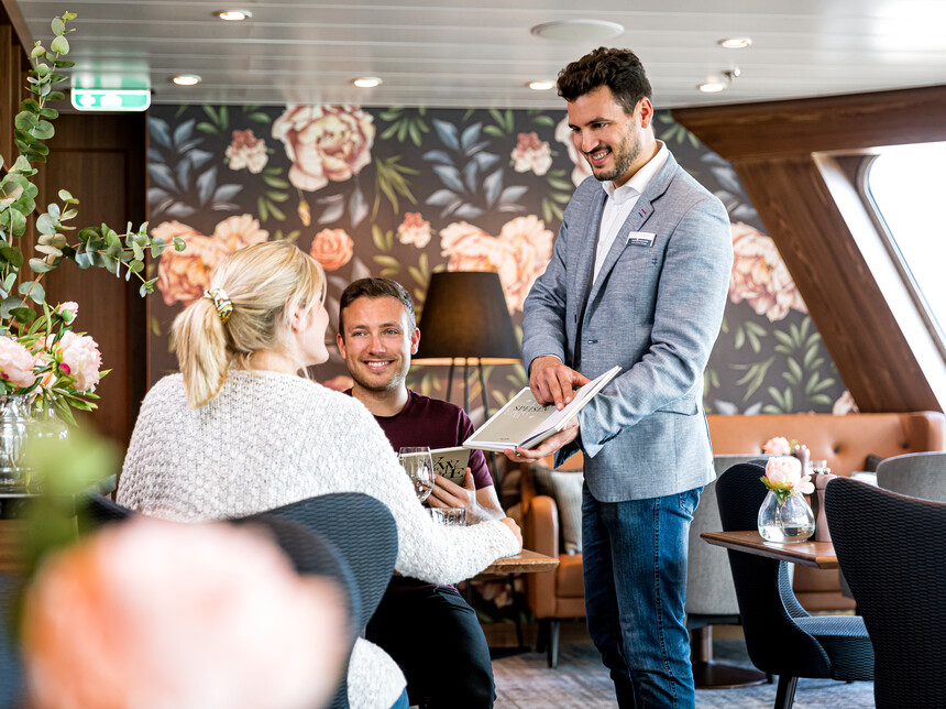 Maitre auf Mein Schiff präsentiert Menü an Gäste im Restaurant an Bord