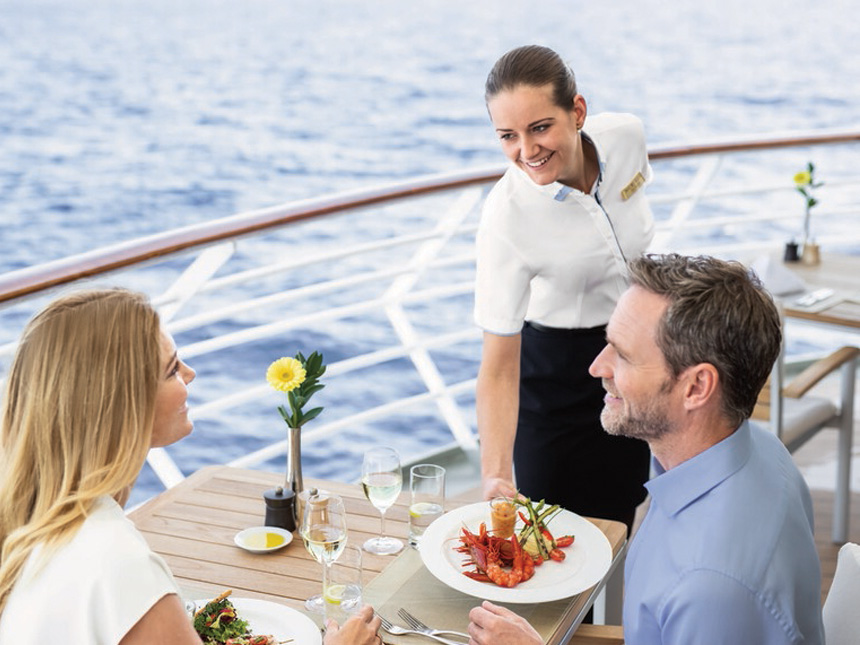 Restaurantfachfrau an Bord von Hapag-Lloyd Cruises serviert mit Blick auf das Meer