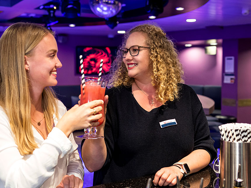 Zwei Crewmitglieder stehen an der Crewbar auf der Mein Schiff und prosten sich mit Cocktail zu